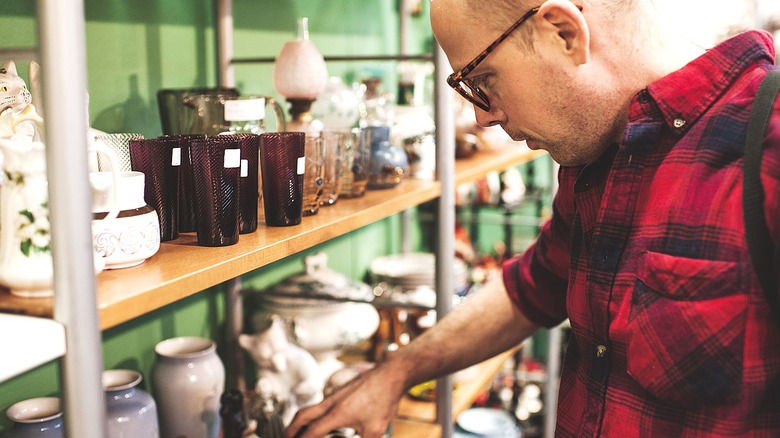 Person in red plaid shirt shopping for glass ware at thrift store