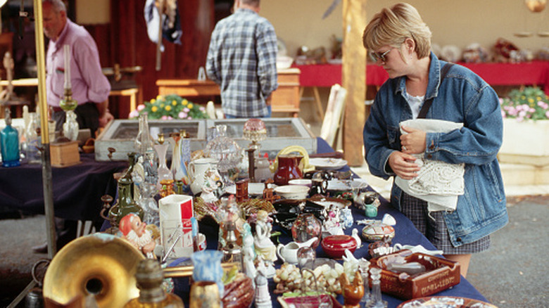 Woman browsing ceramics for sale at an outdoor yard sale or vintage sale while a man looks over at another table