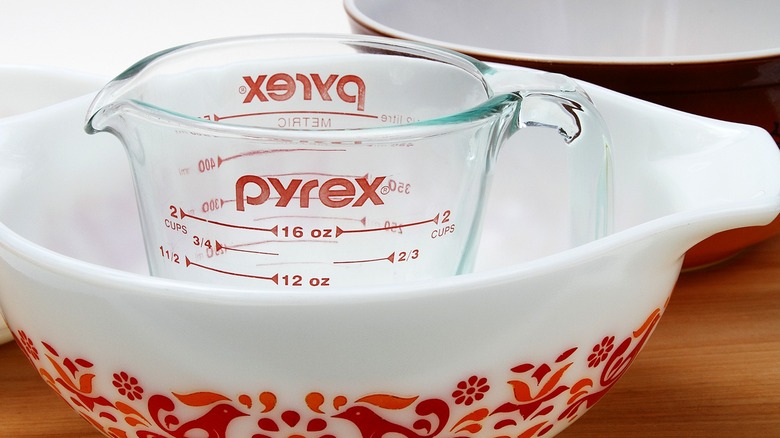 A Pyrex measuring cup inside a Pyrex dish wish a pattern with a solid bowl seen in the background