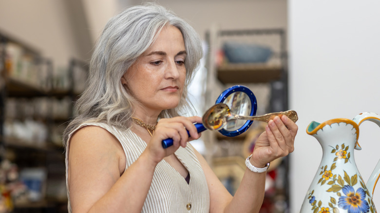 Woman examining a silver spoon with a magnifying glass in an antique store.