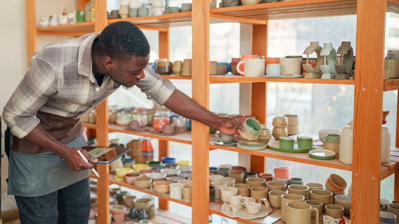 Man with tablet in hand examining pottery at store