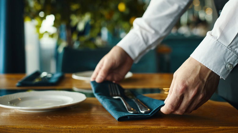 A person arranging a napkin as they set a table.