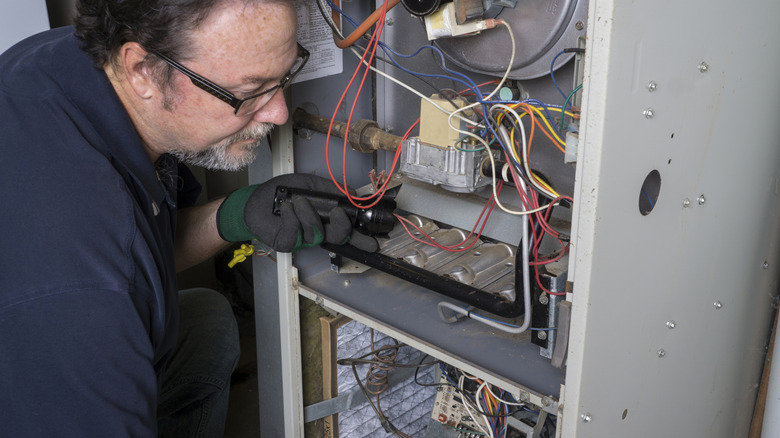 Repair man looking over furnace with flashlight before cleaning