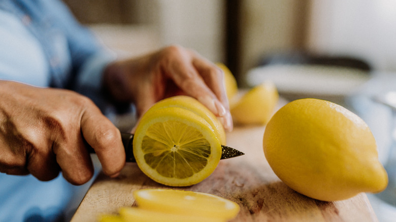 Close-up of a person slicing a fresh lemon with a knife on a wooden cutting board