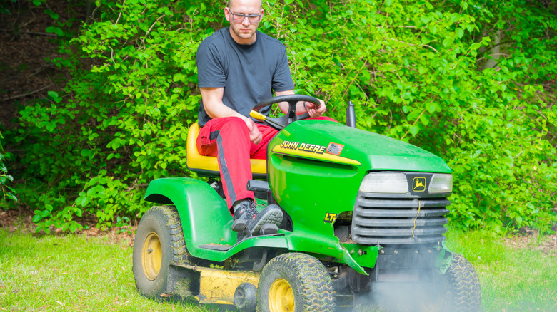 Man riding a lawn mower that's blowing smoke