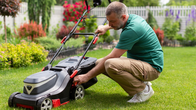 A man in his lawn inspecting his black and grey lawn mower
