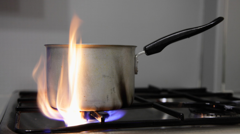 A stainless steel pan on a gas stove hob with high flames