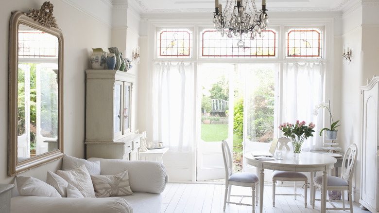 A bright, white living room with an antique mirror, sofa, and table and chairs