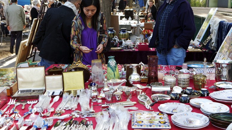 Woman browsing table full of silverware, dishware, and other kitchen items