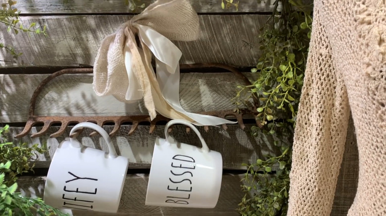 A repurposed garden rake turned into a coffee mug holder with a bow on top.