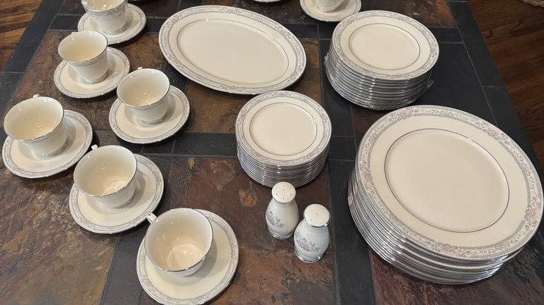 Tabletop covered with pieces of the Lenox Charleston pattern including several teacup and saucers, a stack of plates, an oval serving plate, and salad plates as well as matching salt and pepper shaker.