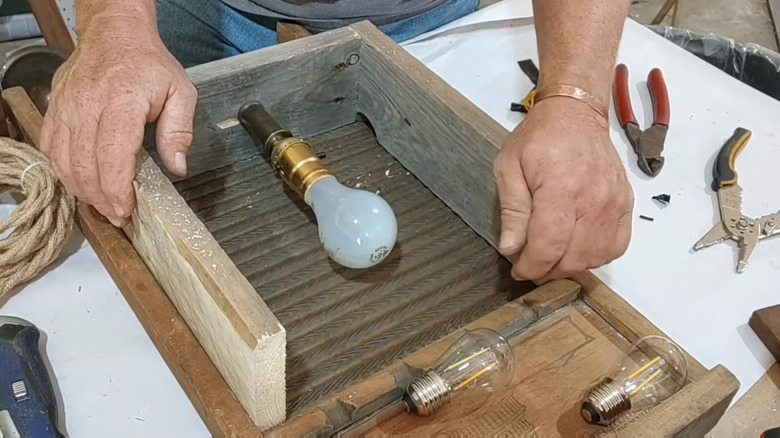 a person crafting a wall sconce with an antique washboard, wood boards and a bulb