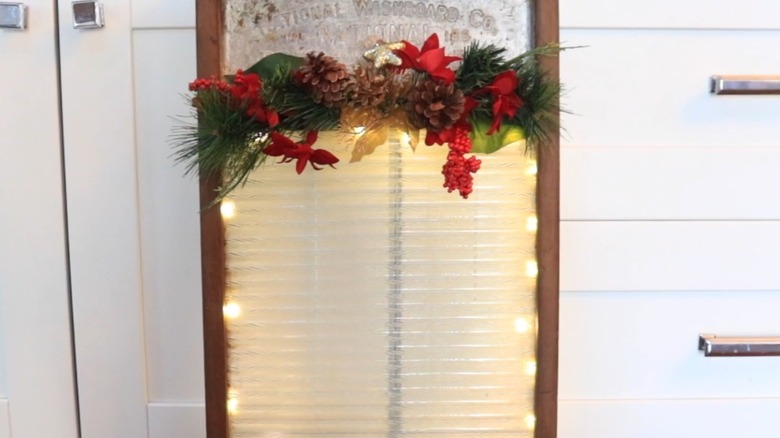 An old washboard converted to Christmas decor with holiday greenery and LED lights