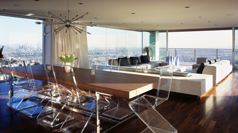 A large wooden dining table with transparent Lucite chairs in a mid-century style open-plan living room.