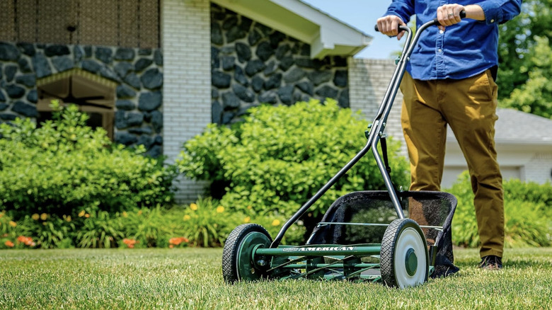 A man pushing a lawn mower with an attached grass catcher.