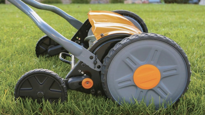 An orange push mower on a bright green lawn.