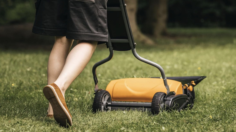 A person pushing an orange Fiskars brand mower on short grass.