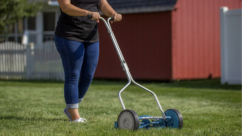 A woman walking behind a simple push mower.