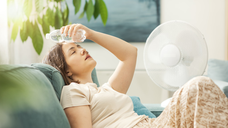Woman sitting in front of fan with water bottle on head