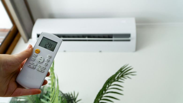 Person adjusting the air conditioning with a remote control for enhanced comfort.