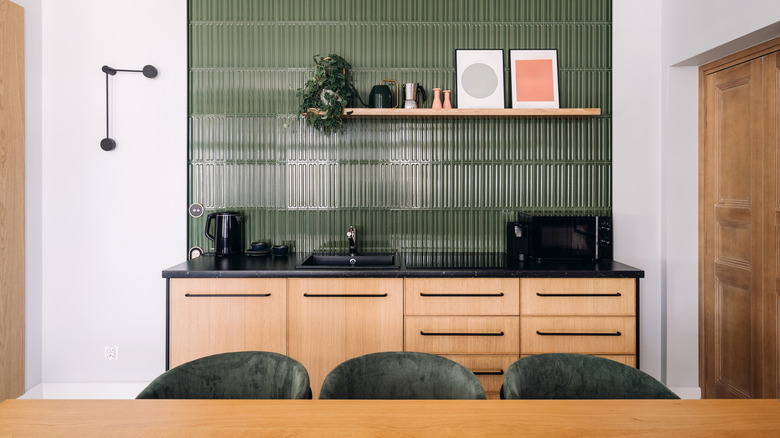 A kitchen with a green tile backsplash and dark black countertops and bar seating