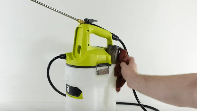 Person wiping the exterior of a Ryobi garden sprayer tank