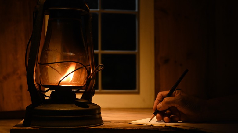 person writing by kerosene lamp