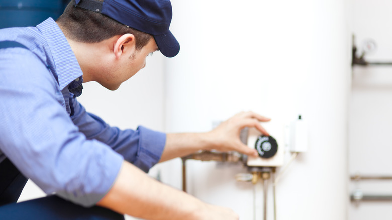 Man in a blue hat and shirt turns water heater off before draining it