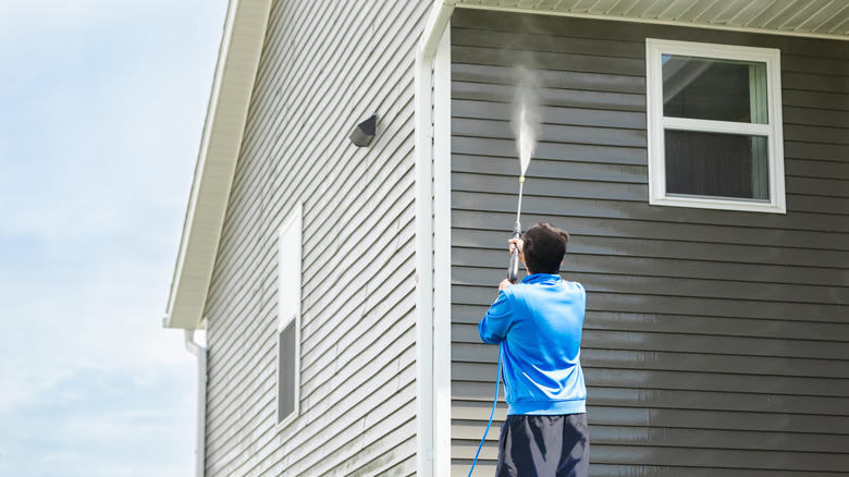 Man pressure washing house