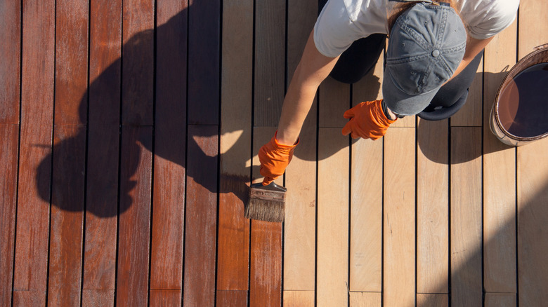 A person stains a wooden deck a rich brown color.