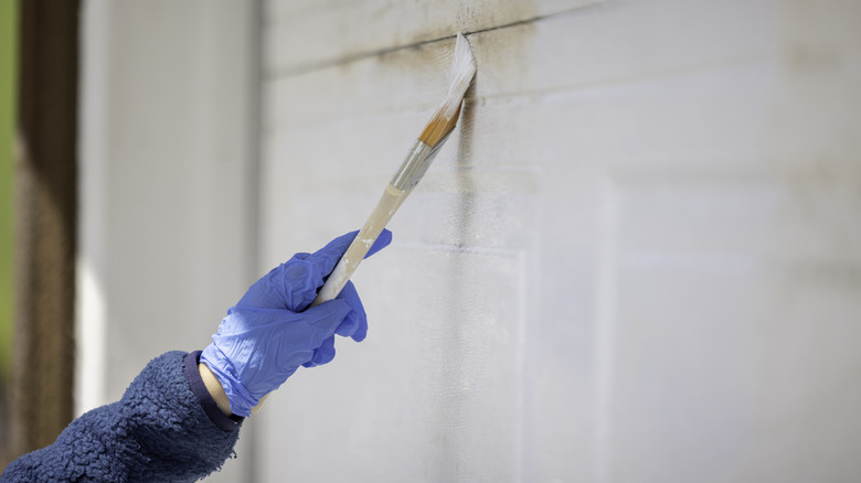 hand wearing blue latex gloves painting garage door white