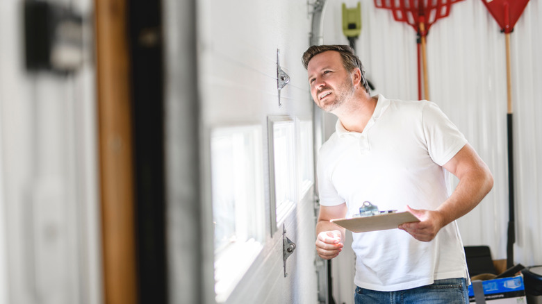 A man with a notepad inspects a white garage door