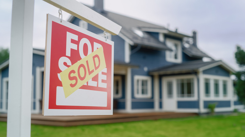 Red For sale sign in front of blue house marked as Sold