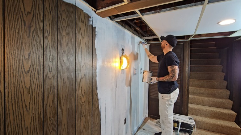 Man brushing primer on wood paneled walls