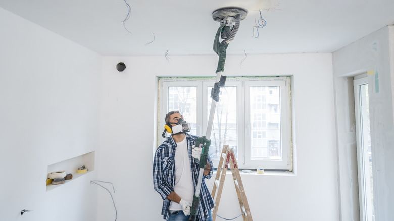 A man wearing PPE sands the ceilings with a vacuum sander