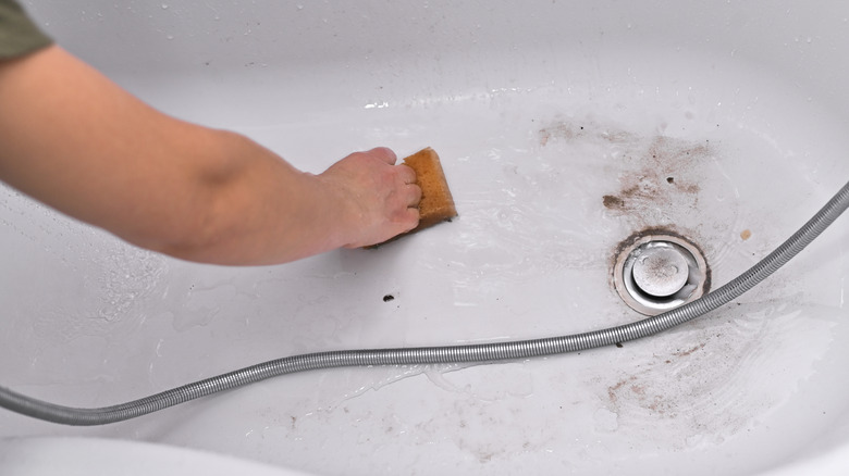 A person cleaning a bathtub with visible stains using a sponge