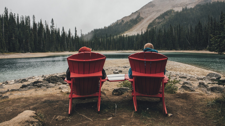 Two people sit in red Adirondack chairs