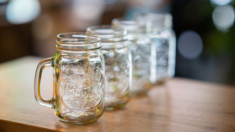 four empty glass jars with handles on a wooden table