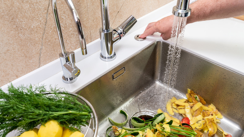 Person's hand turning on garbage disposer to get rid of a sink full of vegetable peels