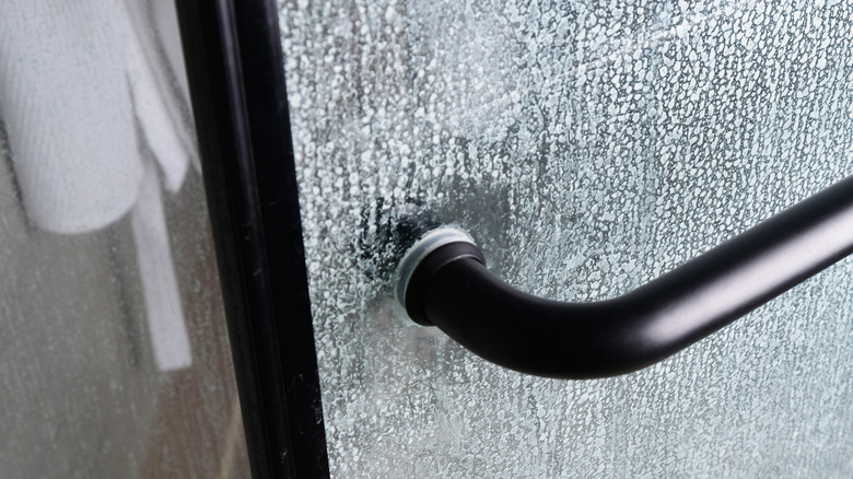 A glass shower door handle with water stains