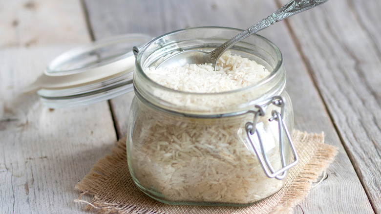open glass jar filled with white rice with silver spoon set on top
