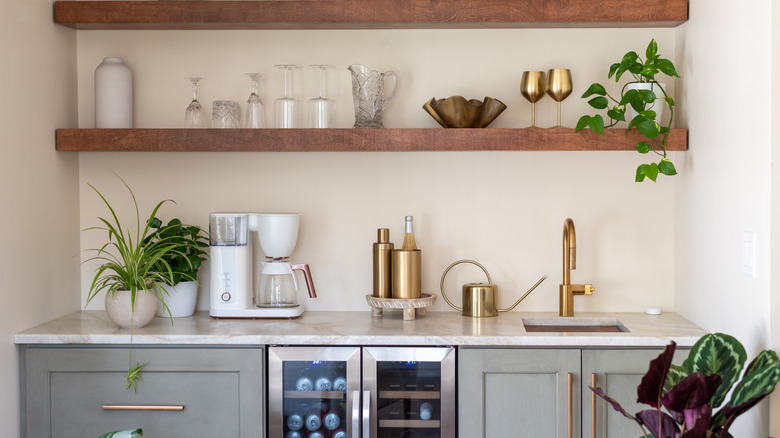 Grey lower cabinets with wine fridge and wood open shelving above, glassware and coffee maker.