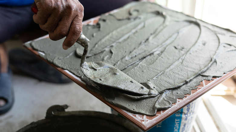 Hand scraping plaster off a hawk with a putty knife