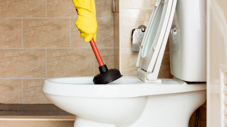 Gloved hand plunging a clogged toilet