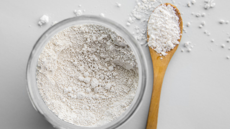 A clear bowl full of diatomaceous earth with a filled wooden spoon next to it.