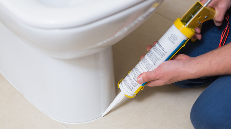 person applying caulk on toilet