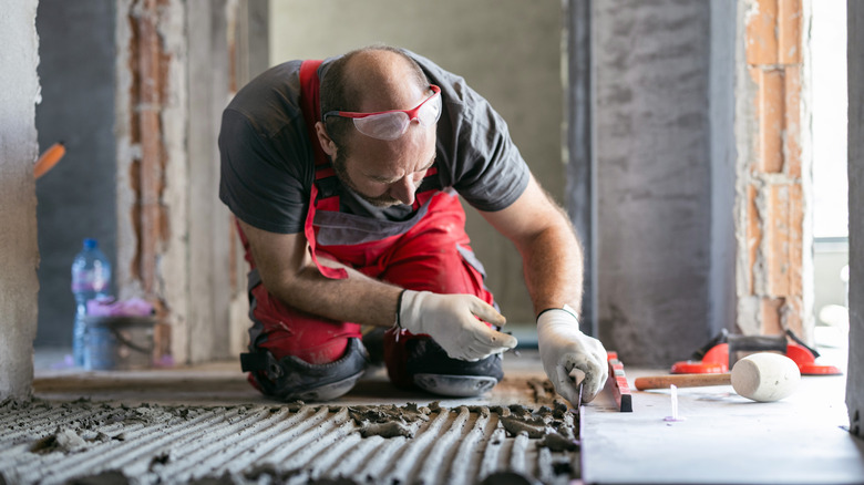 A male tile worker with working gear leveling a newly installed tile.