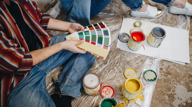 People sitting on floor looking at paint swatches, surrounded by paint cans