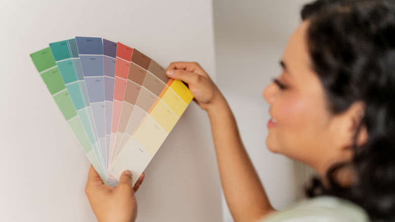 Close-up of a woman holding paint swatches against a white wall