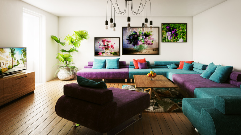 A living room with a wrap around colorful couch with wire chandelier and gallery wall